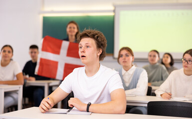 High school teacher tells students about Denmark and holds a Denmark flag in her hands.