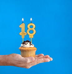 Hand delivering birthday cupcake - Candle number 18 on blue background