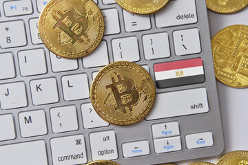 national flag of egypt on the keyboard with bitcoin coins on a grey background.