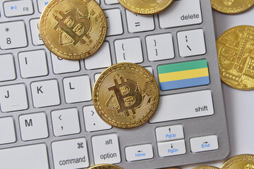 national flag of gabon on the keyboard with bitcoin coins on a grey background.