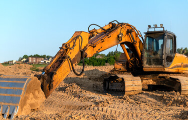 Front view of heavy-duty yellow color excavator with shovel at sunny day.