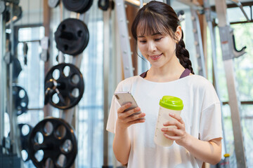 プロテインを持ちながらスマートフォンを使う女性