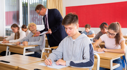 Fototapeta premium Friendly teacher man helping students during lesson in schoolroom