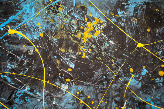 Wall with blue and yellow paint splashes. Dark canvas with abstract splashes and drops of bright yellow and light blue dye. Modern art piece: abstract stains of paint on black background