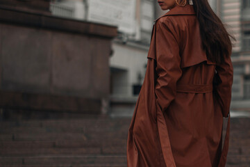 Fancy details of autumn long brown leather trench coat. Street style casual clothing. Woman walking alone in the city.