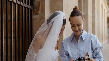 Photographer showing pictures to a model young bride. Action. Wedding photosession outdoors.