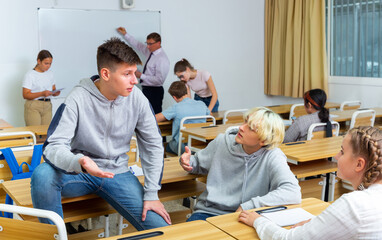 Positive teen students communicating during recess between lectures in classroom