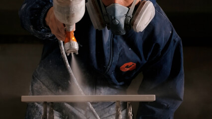 Close up of a male carpenter hands spraying varnish or primer using compressed air on a wooden...