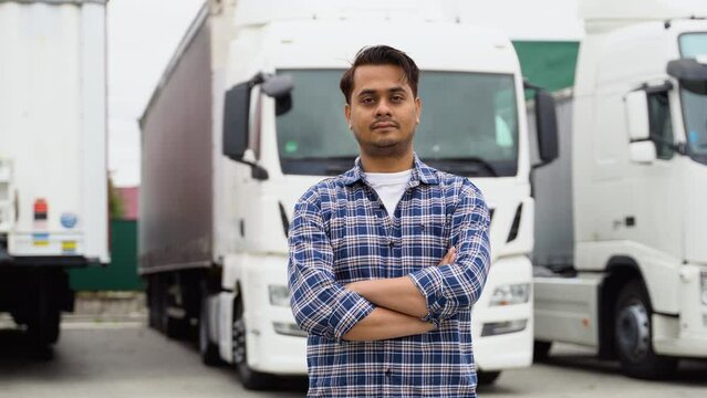 Indian truck driver standing with arms crossed on truck parking lot and looking at camera. Truck driver job
