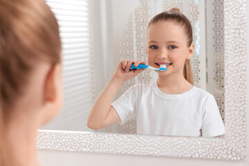 Cute little girl brushing her teeth with plastic toothbrush near mirror in bathroom