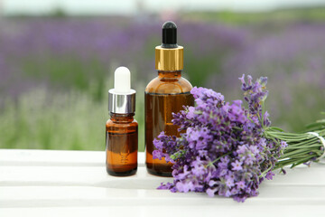 Bottles of essential oil and lavender flowers on white wooden table in field