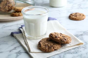 Tasty chocolate chip cookies and glass of milk on white marble table, closeup