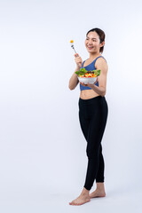 Fototapeta na wymiar Young sporty Asian woman in sportswear holding salad bowl fill with vibrant of fruit and vegetable. Natural youthful and fit body lifestyle with balance nutrition on isolated background. Vigorous