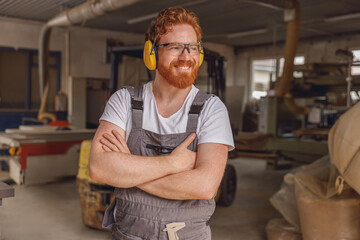 Smiling woodworker with crossed hands standing on the background on carpentry workshop