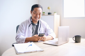 Happy young Asian doctor holding smart phone ready for online telemedicine consultation in medical...