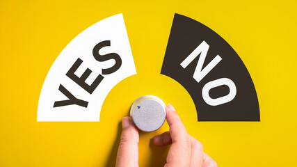 Hand adjusting the volume selector for choosing YES or NO on isolated yellow background. Questionnaire question and answer concept. - obrazy, fototapety, plakaty