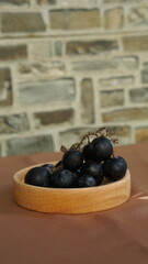 a bunch of black grapes in a round wooden container. light brown background