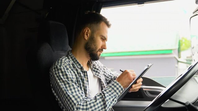 Delivery man with cardboard box checking list in truck. Courier sitting in truck and checking the delivery list