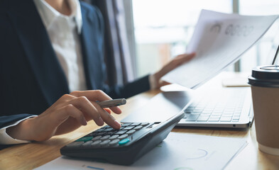 Accountant using calculator with financial documents on desk office.