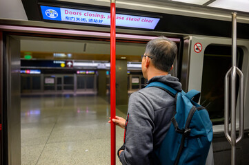Man standing by the open door of the airport rail link. The neon board overhead with messages in...
