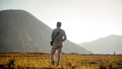A hiker  share a moment gazing out over a beautiful summer field of Bromo Mountain landscape. east...