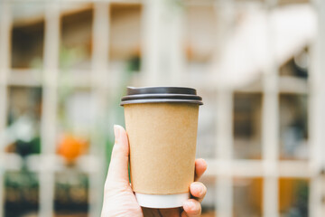 A man's hand holding a cup of coffee in the morning with red brick background. Concepts of...