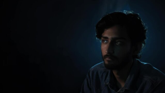 Close-up shot of a man in a denim shirt sitting on a couch at night in a smoky dark environment, HD stock footage.