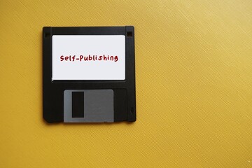 Floppy disk on yellow copy space with text SELF-PUBLISHING, act of writer publish piece of creative...