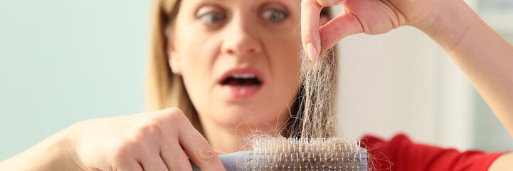 Scared blonde woman collects fallen hair tangled in brush