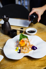 Prawn tartar with tomato, red onion and flowers with hand pouring soja sauce on the background. Japanese restaurant food concept vertical stills.