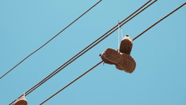 Old sports shoes dangle by their laces over a high electricity line.