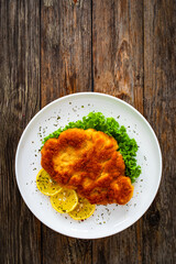 Crispy breaded seared chicken cutlet with lemon slices and fresh vegetables on wooden table
