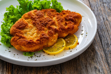 Crispy breaded seared chicken cutlet with lemon slices and fresh vegetables on wooden table
