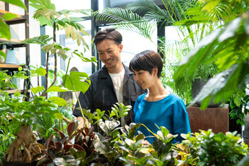 A stylish Asian man and woman couple happily shop for houseplants in a plant shop. Environmental considerations. Sustainability.Seasonal shopping.
