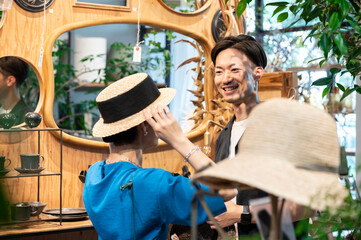 Beautiful Asian heterosexual couple shopping for hats in a trendy shop with lots of plants. They look in the mirror and smile at each other. Urban life.