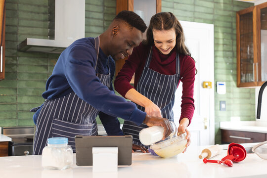 Happy diverse couple baking together in kitchen, using tablet at home