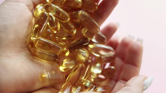 Close-up medicine yellow transparent pills, omega 3 fish oil capsules, vitamin D. A young woman pours yellow transparent capsules from hand to hand. The concept of health, vitamins, and medicine