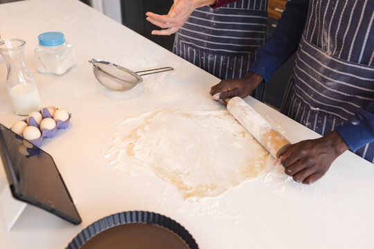 Midsection of diverse couple baking together in kitchen, using tablet at home