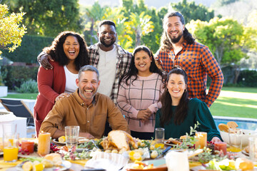 Happy diverse male and female friends posing during thanksgiving celebration meal in sunny garden