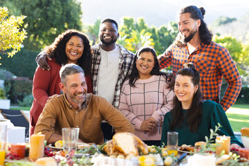 Happy diverse male and female friends posing during thanksgiving celebration meal in sunny garden