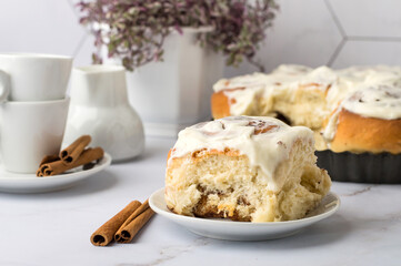 Fresh Cinnabon rolls on the kitchen table, cinnamon sticks, coffee cups and a milk jug. Homemade cinnamon rolls.