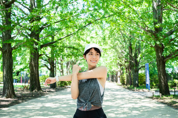 Young Asian woman stretching arms and shoulders while running in a park in the morning. Health and...