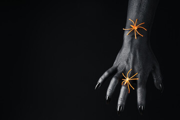 Orange spiders on black female hand on black background, space for text