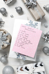 Notepad with list, decorations and gift boxes on light background, top view