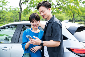 A couple smiling and looking at their smartphone next to a car.