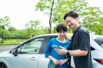 A couple smiling and looking at their smartphone next to a car.