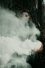 A young woman in a Gothic gloomy image of a witch surrounded by smoke, a pumpkin in her hands. Halloween costume. Vertical photo.