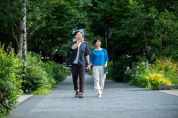 A beautiful couple, a man and a woman, are walking happily hand in hand through a green shopping commercial area. They are smiling and chatting. Urban dwellers. Healthy lifestyle.