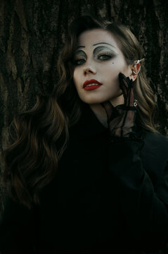 Portrait of a young woman in the Gothic gloomy image of a witch in the forest. Halloween costume. Vertical photo.