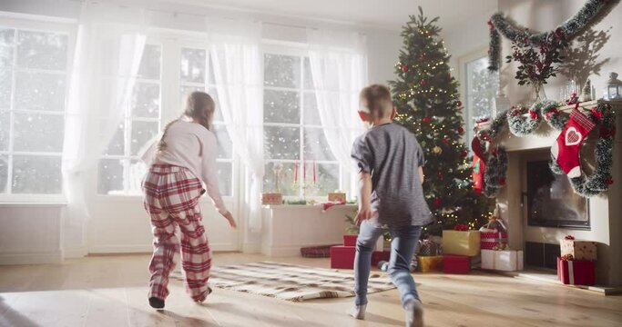 Slow Motion of Cute Kids in Pajamas Running To Get Their Gifts On Christmas Bright Morning. Happy Kids Getting Surprised While Opening Holiday Wrapped Gift Boxes, Receiving New Toys from Santa 